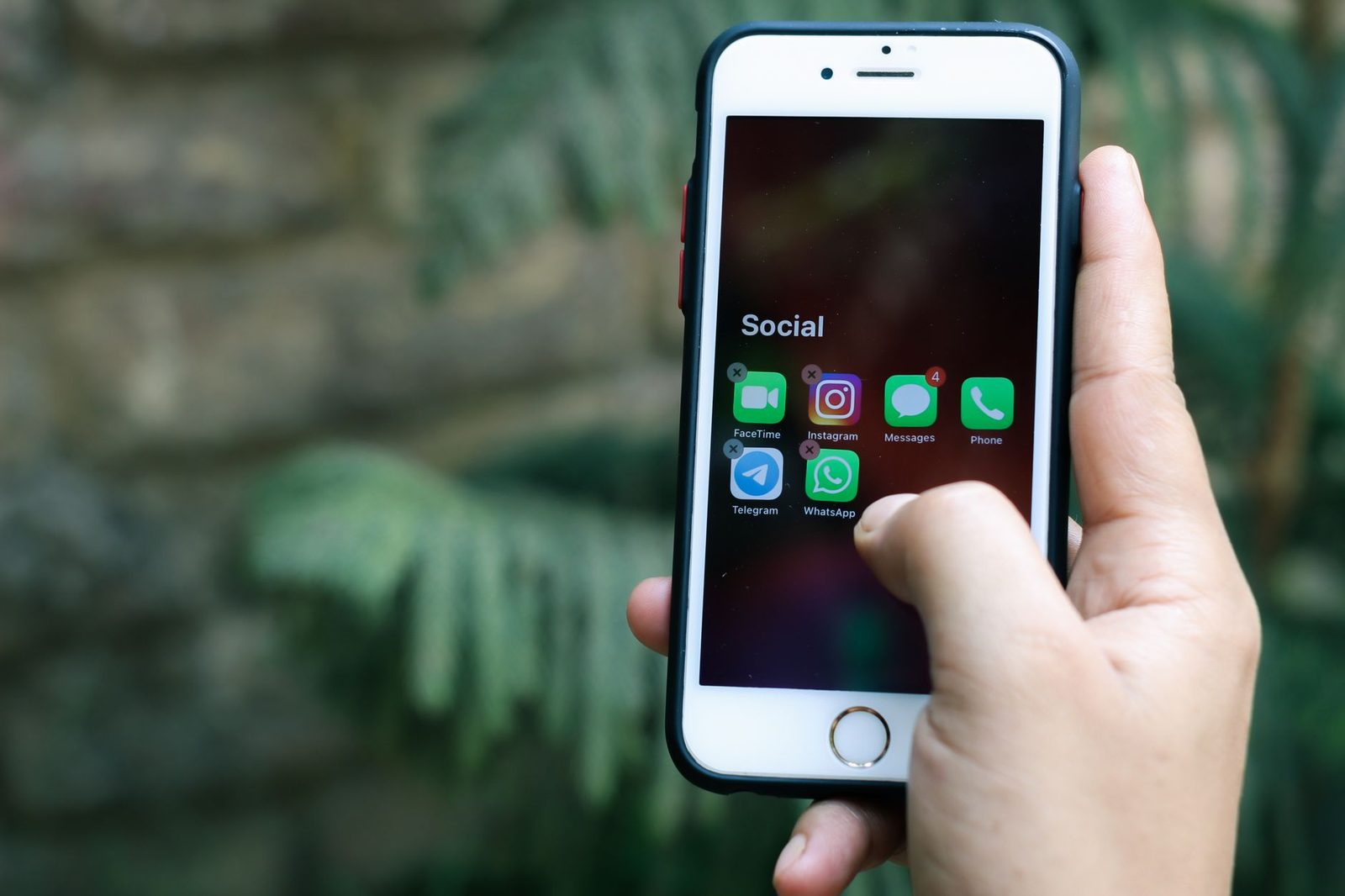 Hand hält ein Smartphone, auf dem ein Ordner „Social" mit Messenger- und Videoanruf-Apps zu sehen ist