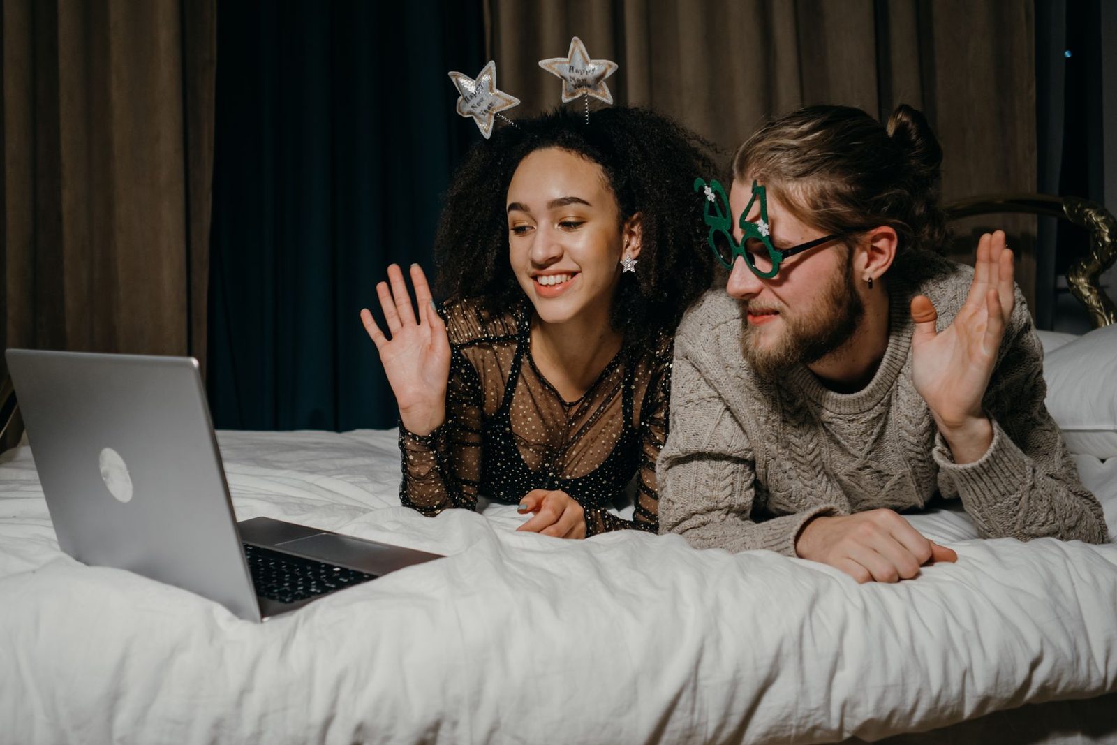Ein Paar liegt auf einem Bett und winkt während eines Videoanrufs in einen Laptop