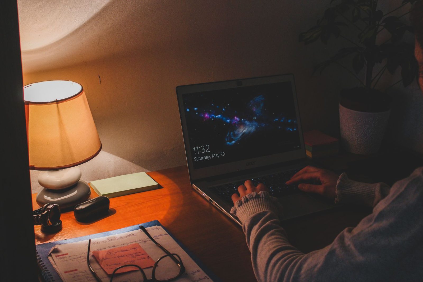 Person tippt abends an einem von einer Lampe beleuchteten Schreibtisch auf einem Laptop mit Webcam
