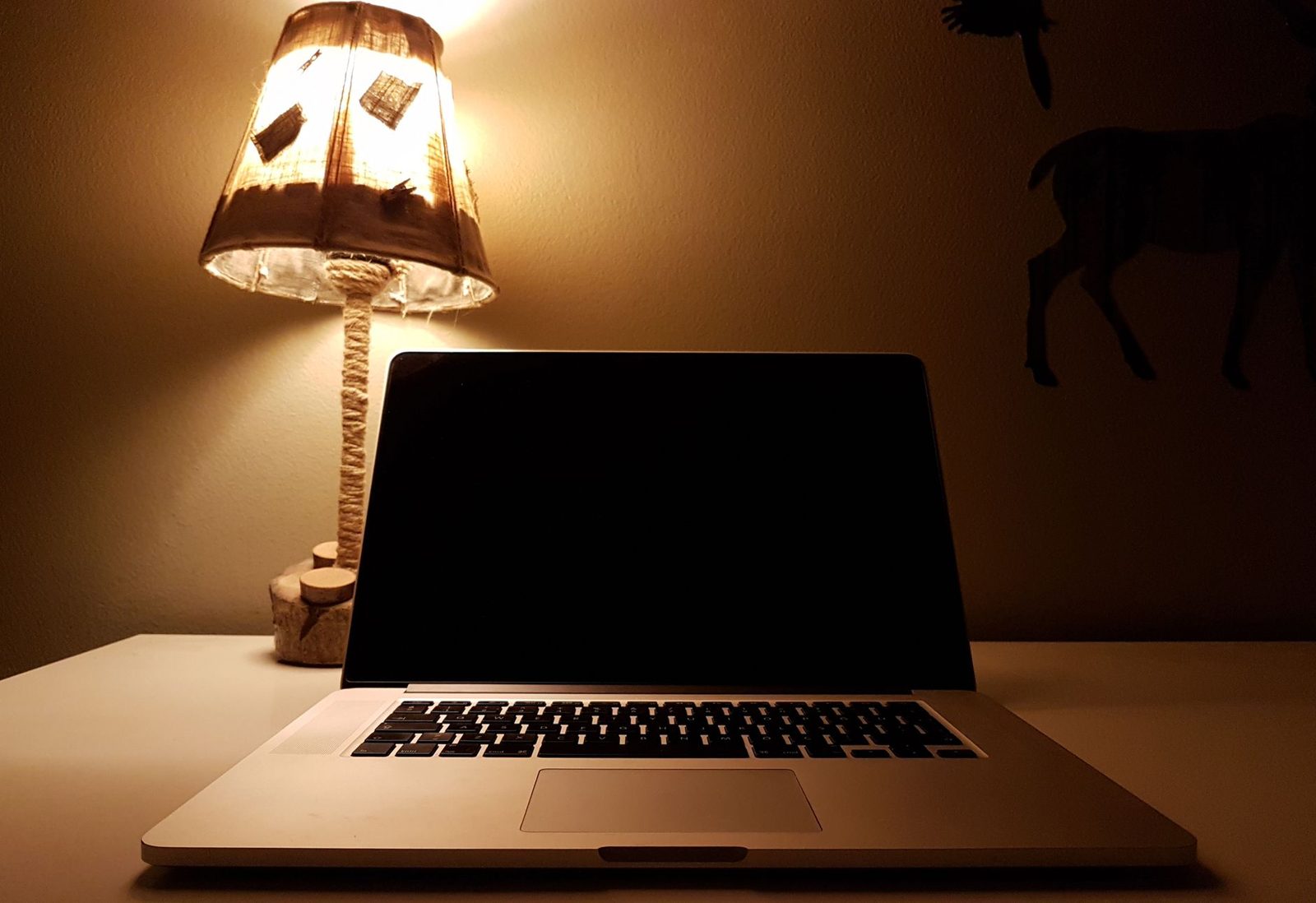 Aufgeklappter Laptop mit schwarzem Bildschirm auf einem Schreibtisch, beleuchtet von einer Nachttischlampe in einem dunklen Raum