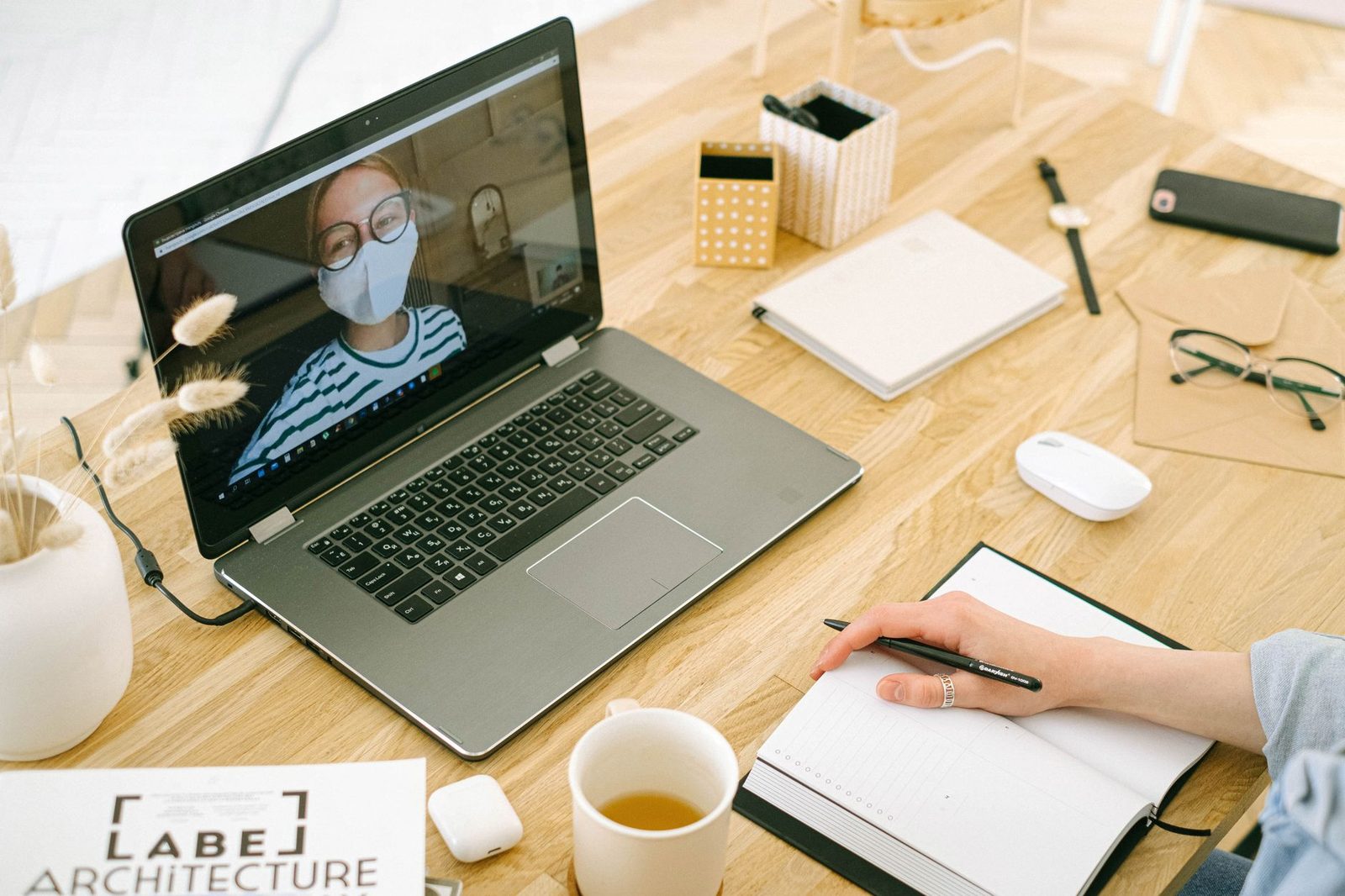 مكالمة فيديو على حاسوب محمول موضوع على مكتب خشبي، مع دفتر وقلم وكوب شاي