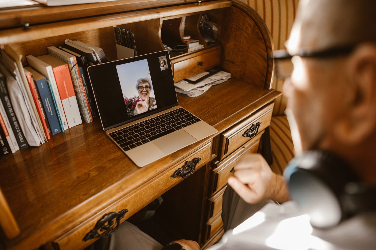 Älterer Mann mit Kopfhörern in einem Videoanruf an einem Laptop auf einem Holzschreibtisch