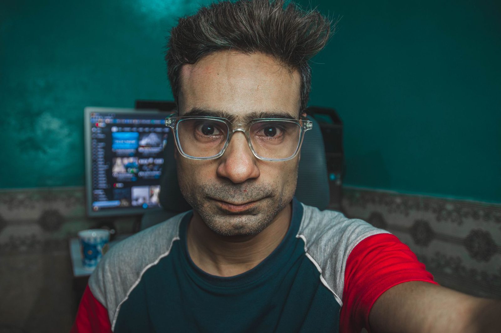 Uomo con gli occhiali si fa un selfie davanti allo schermo di un computer che mostra una finestra di video chat