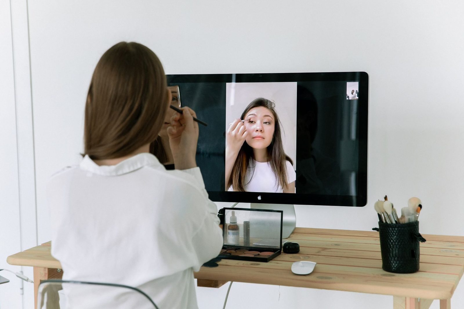 Woman seen from behind in front of a computer screen showing another woman on a video call