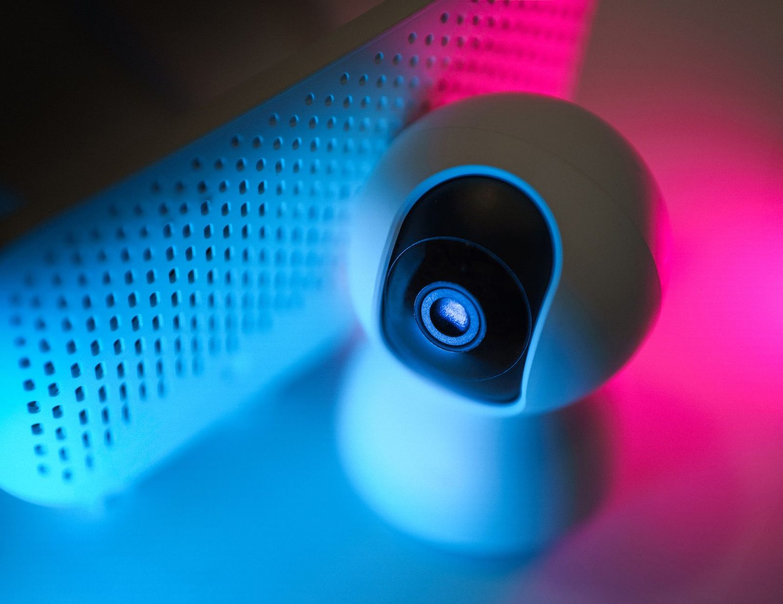 Weiße Webcam in Nahaufnahme neben einem Lautsprecher, beleuchtet von blauem und rosafarbenem Licht