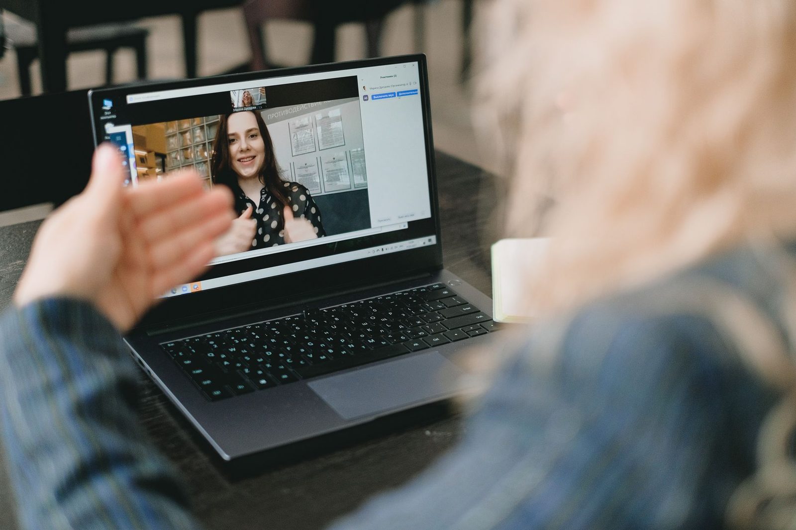 Person am Laptop in einer Videokonferenz mit einer lächelnden jungen Frau auf dem Bildschirm