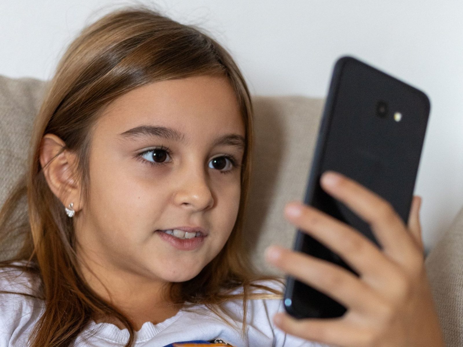 Junges Mädchen sitzt auf einem Sofa und blickt auf das Display eines Smartphones in ihrer Hand