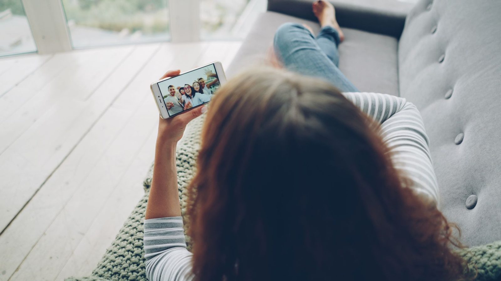 Eine Person liegt auf einem Sofa und schaut sich einen Videoanruf auf ihrem Smartphone an.