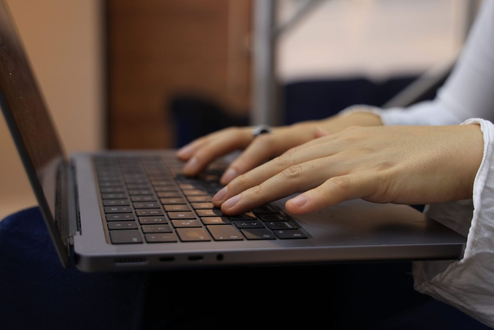 لقطة قريبة ليدَي امرأة تكتبان على لوحة مفاتيح حاسوب محمول موضوع على ركبتيها